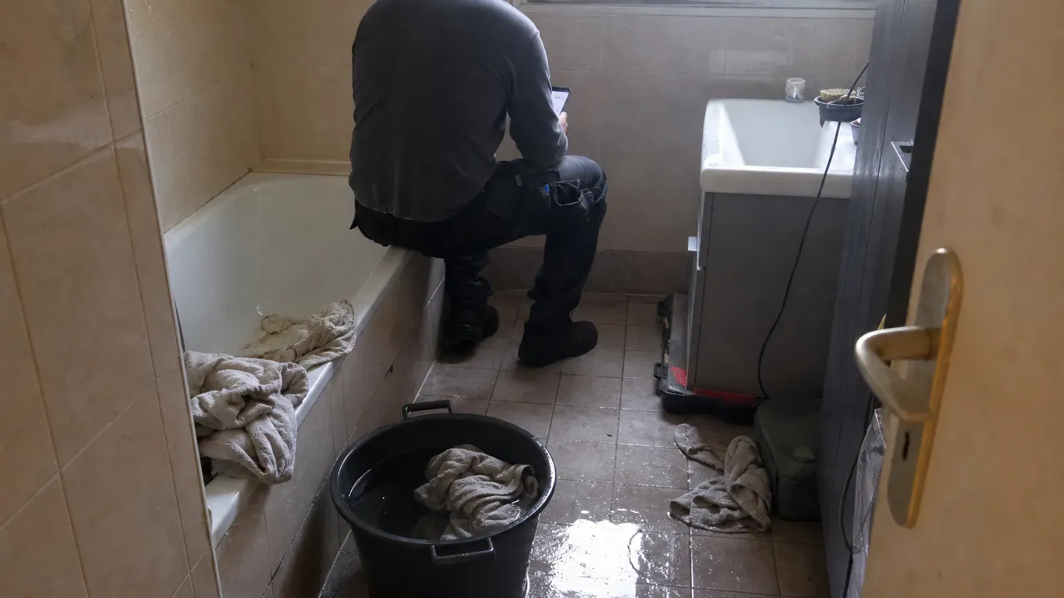 Salle de bains inondée et occupant au téléphone pour déclarer un dégât des eaux soumis à franchise
