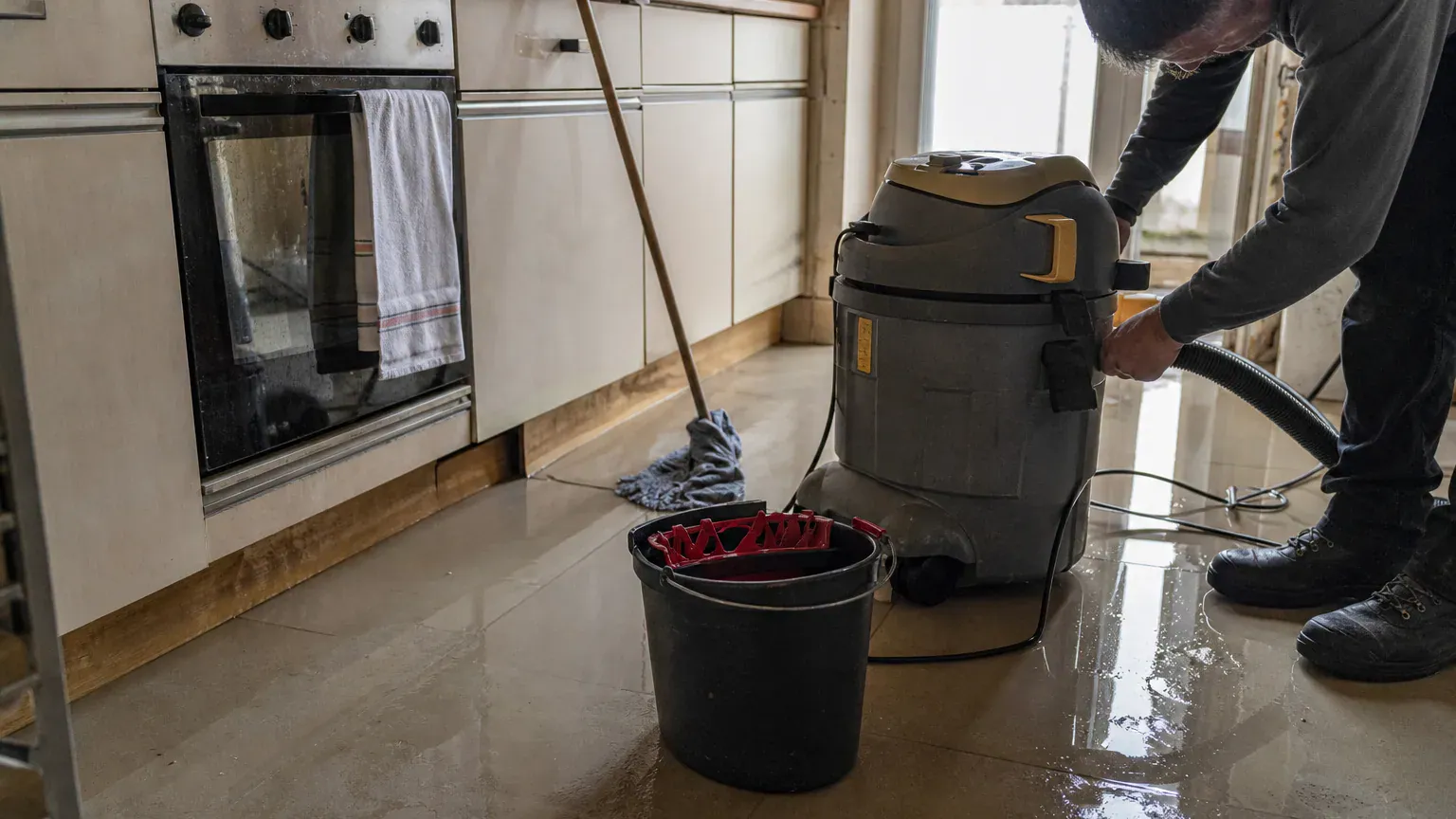 Serpillière de particulier et aspirateur à eau professionnel côte à côte dans une cuisine inondée