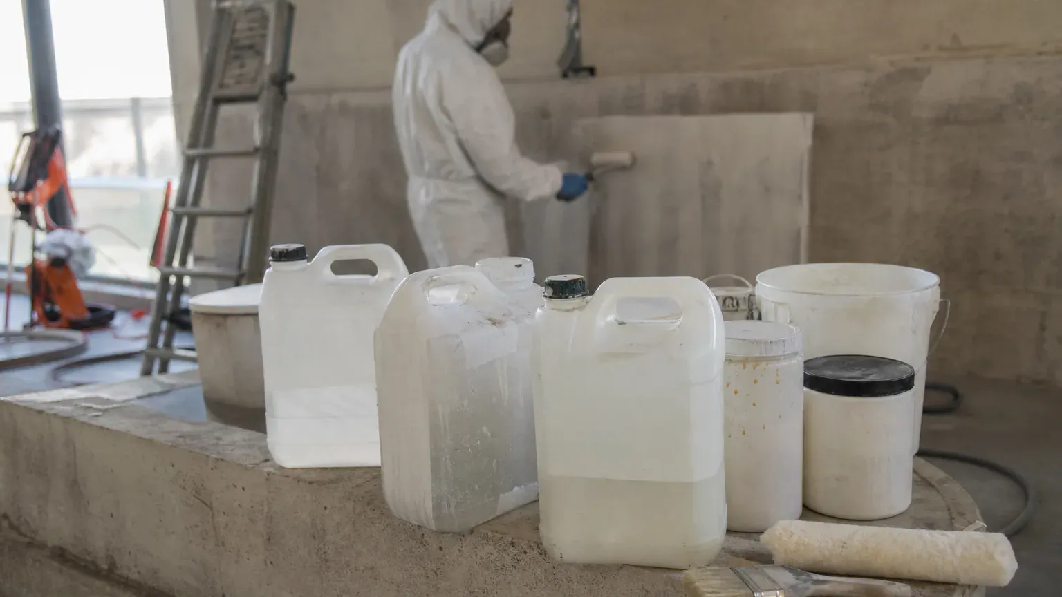 Bidons de produits anti-graffiti, rouleau et pinceau posés sur un muret avant application