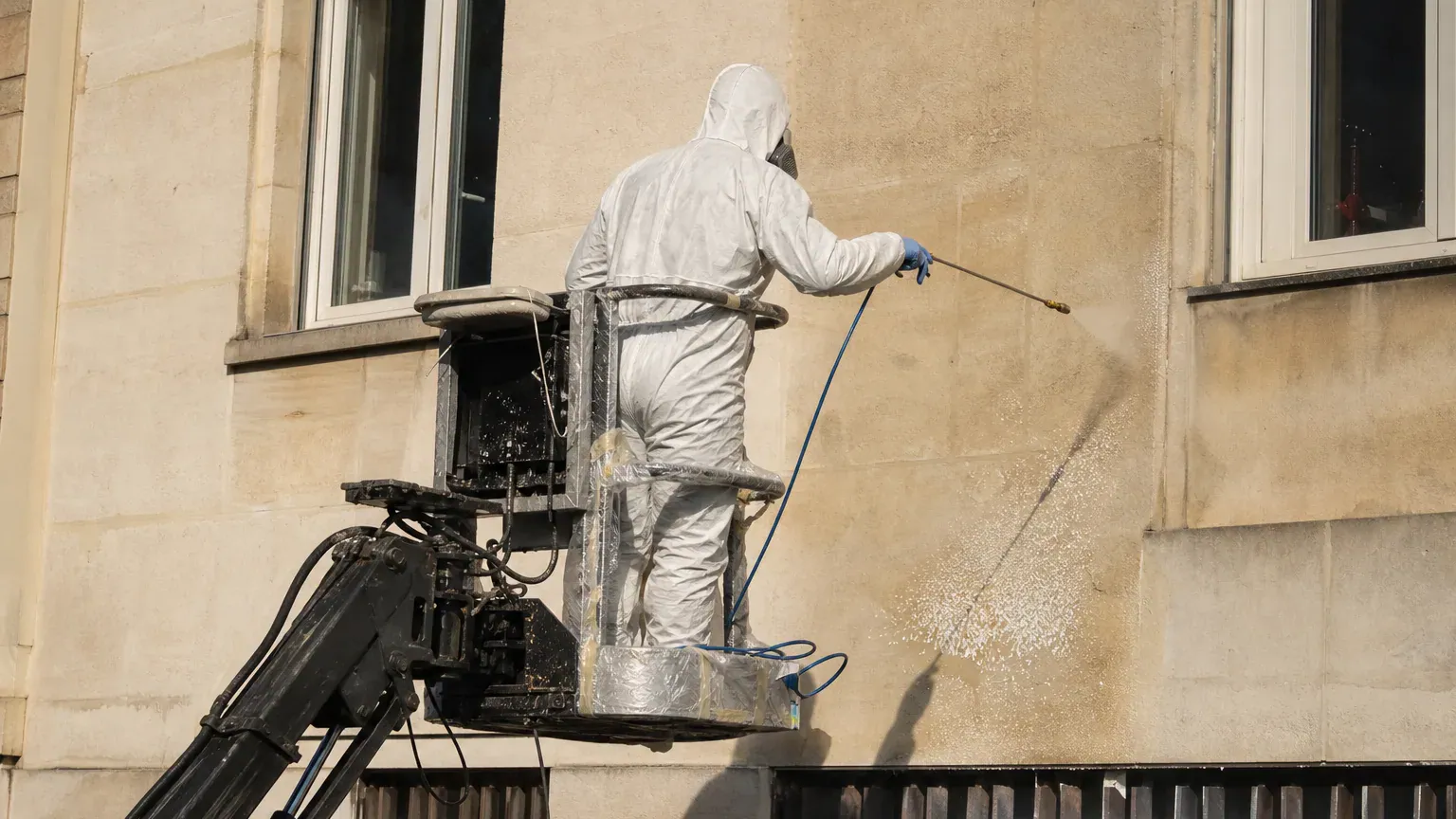 Technicien sur nacelle pulvérisant une protection anti-graffiti sur une façade en pierre claire