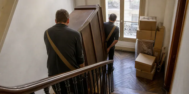 Armoire descendue dans un escalier d'immeuble par deux professionnels, service de débarras