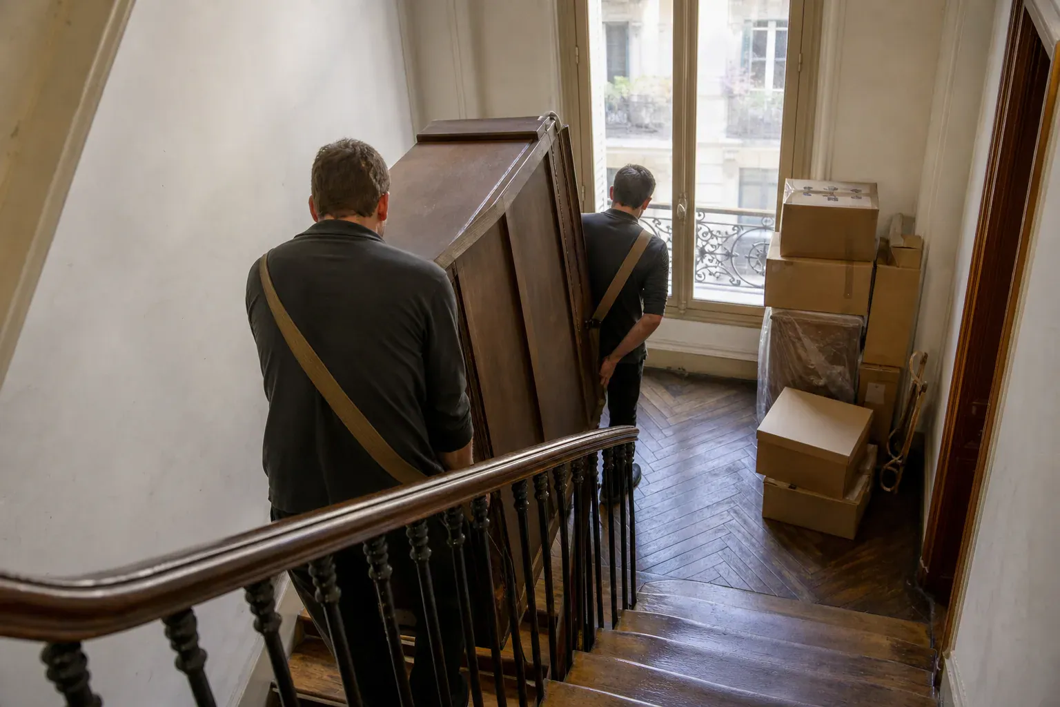 Deux professionnels descendant une armoire dans l'escalier d'un immeuble parisien lors d'un débarras