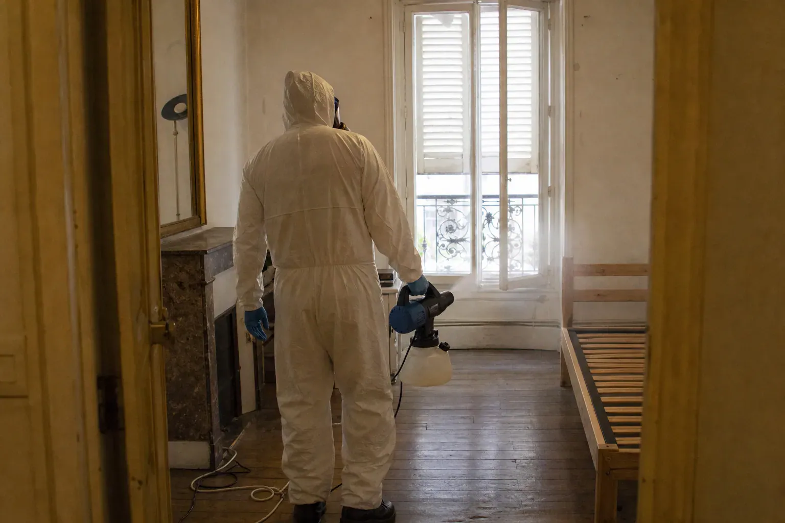 Technicien en combinaison désinfectant une chambre d'appartement parisien lors d'un nettoyage après décès