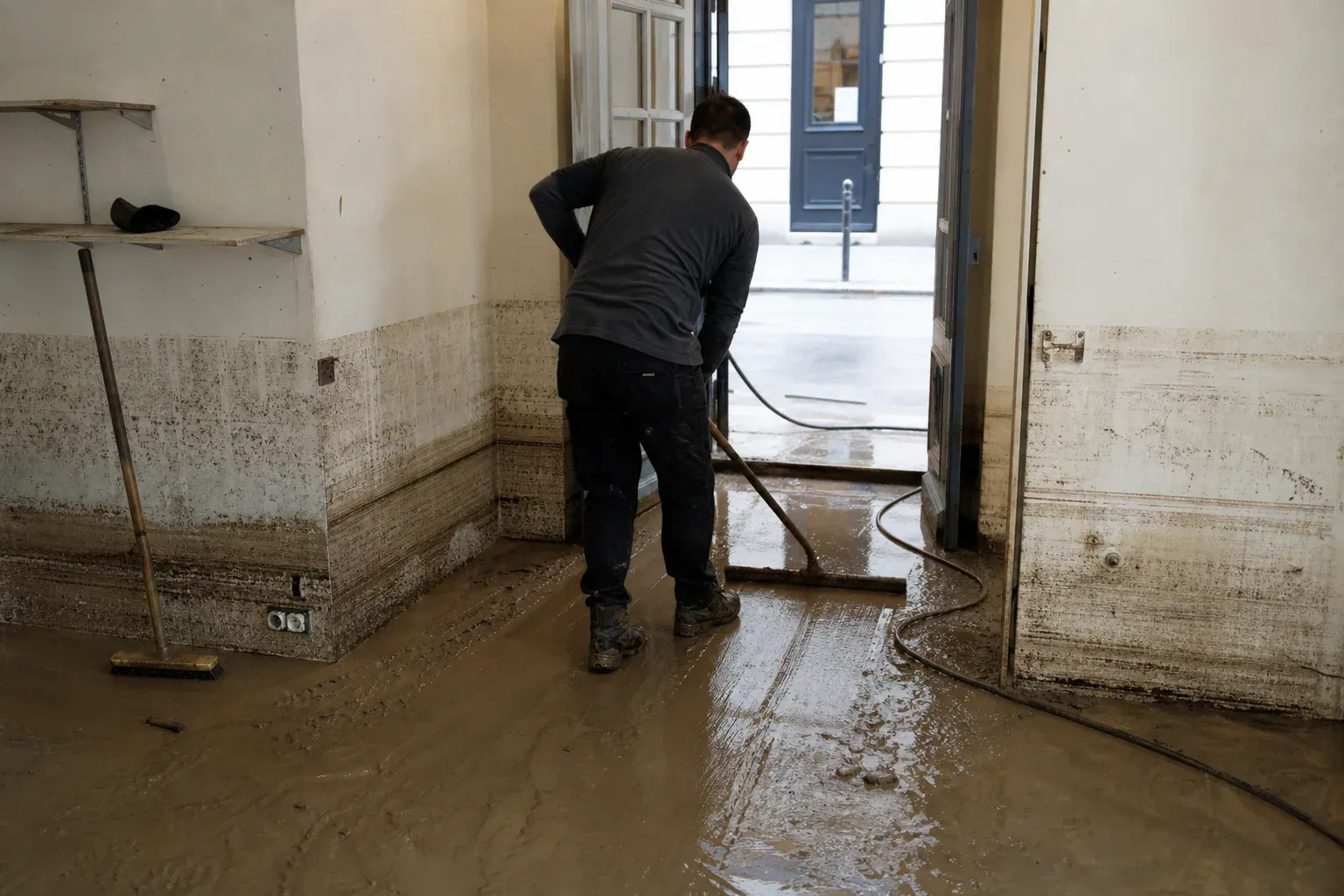 Technicien poussant la boue à la raclette au rez-de-chaussée d'un logement parisien après une inondation