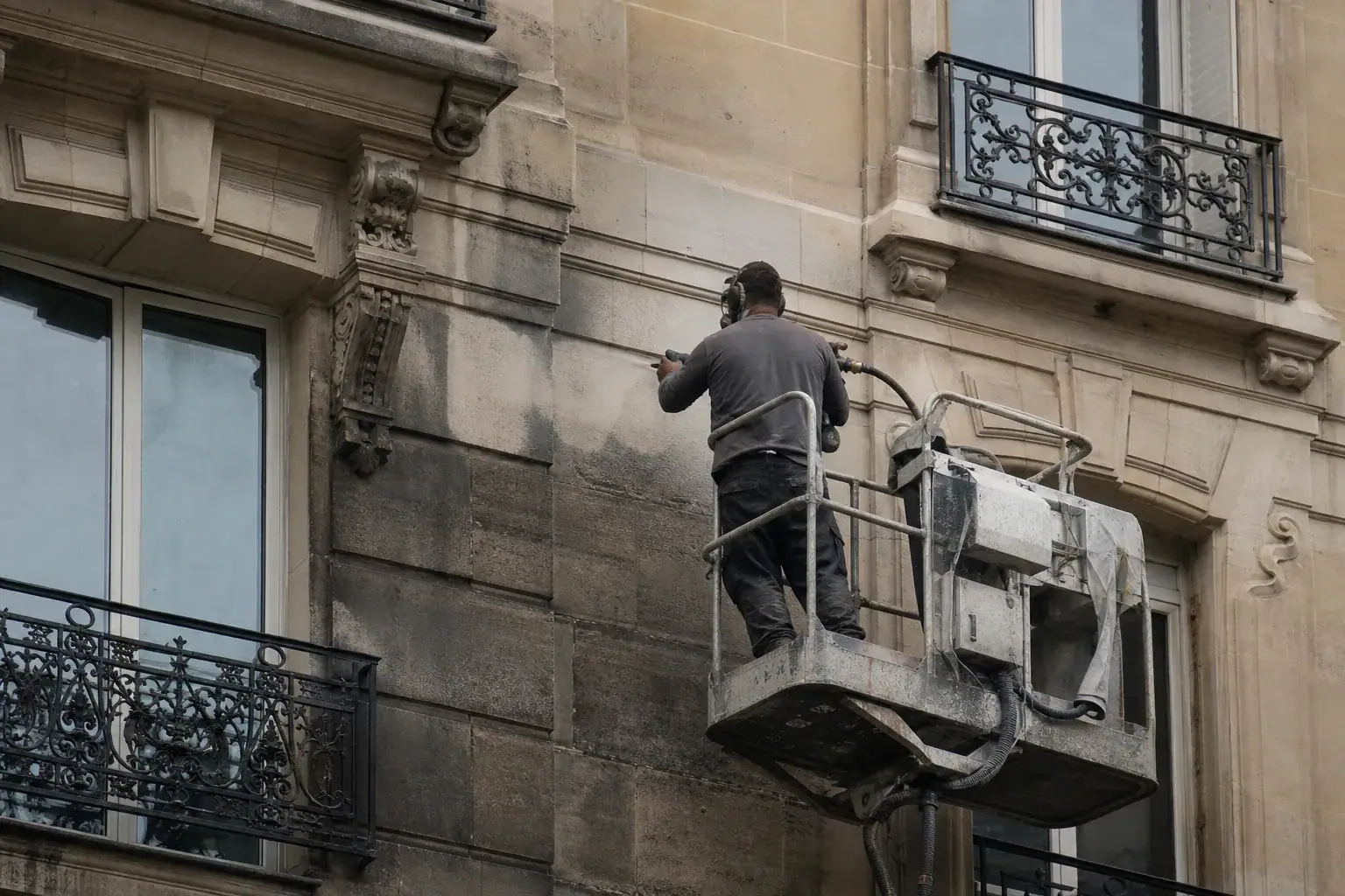 Technicien sur nacelle nettoyant par gommage la façade en pierre d'un immeuble parisien