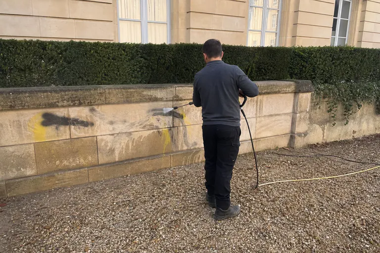Rinçage d'un graffiti sur un muret en pierre de taille d'une résidence des Yvelines