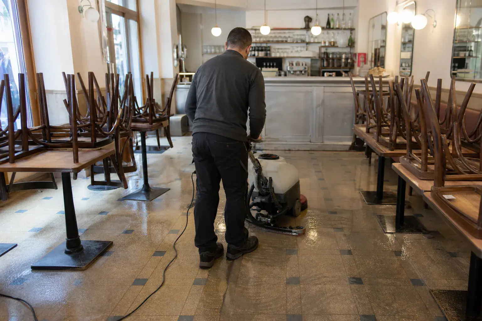 Nettoyage du sol d'un restaurant parisien fermé après un sinistre, chaises retournées sur les tables