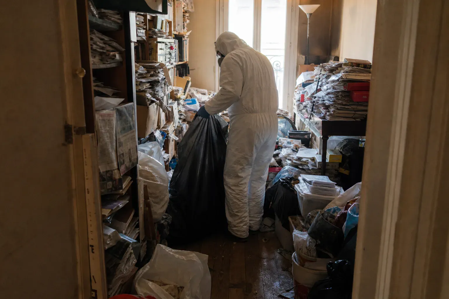 Technicien en combinaison désencombrant un appartement parisien envahi d'objets, syndrome de Diogène